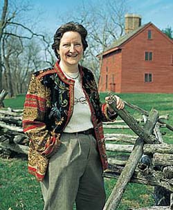 Margo Burns standing near a fence with a farmhouse in the background